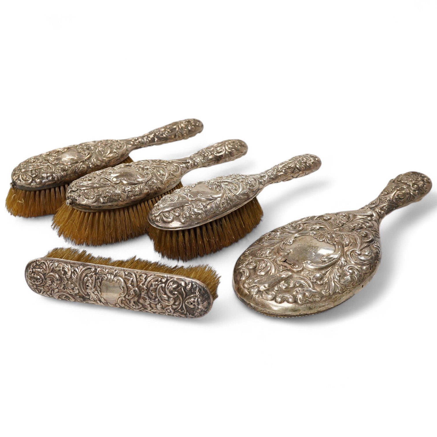 A late Victorian embossed silver four piece dressing table mirror and brush set, by William Comyns, London, 1891/5 and a similar clothes brush.